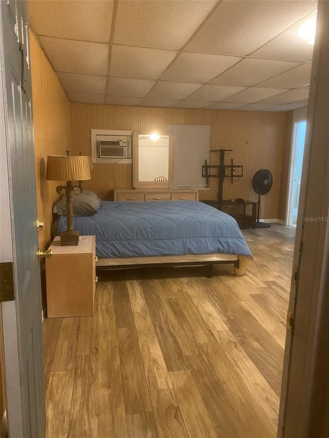 bedroom featuring wood-type flooring, a paneled ceiling, and a wall mounted air conditioner