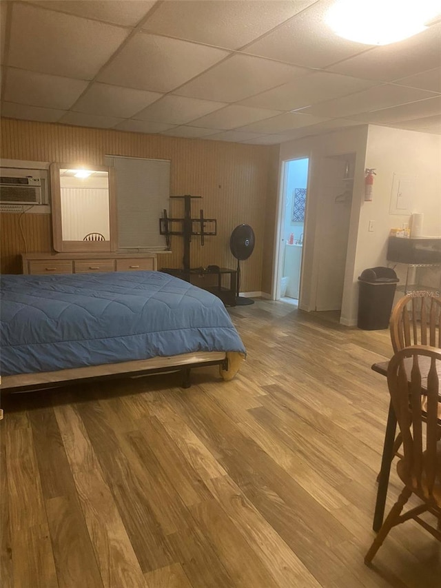 bedroom with wood-type flooring, a wall unit AC, and a paneled ceiling