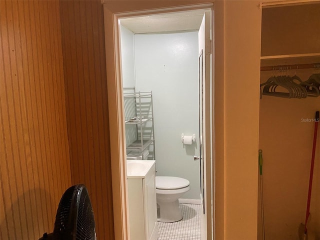 bathroom featuring tile flooring, vanity, wooden walls, and toilet