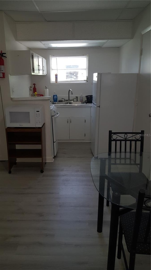 kitchen with white appliances, white cabinets, light wood-type flooring, sink, and a paneled ceiling