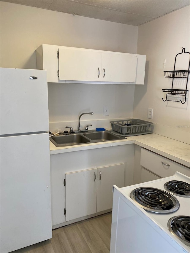 kitchen featuring white refrigerator, range, white cabinets, sink, and light wood-type flooring