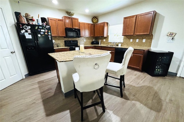 kitchen featuring a center island, a kitchen breakfast bar, light wood-type flooring, black appliances, and tasteful backsplash