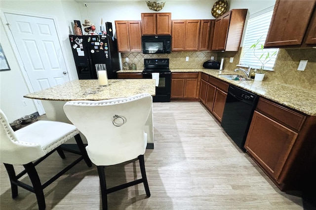 kitchen featuring black appliances, sink, light stone counters, a breakfast bar area, and tasteful backsplash