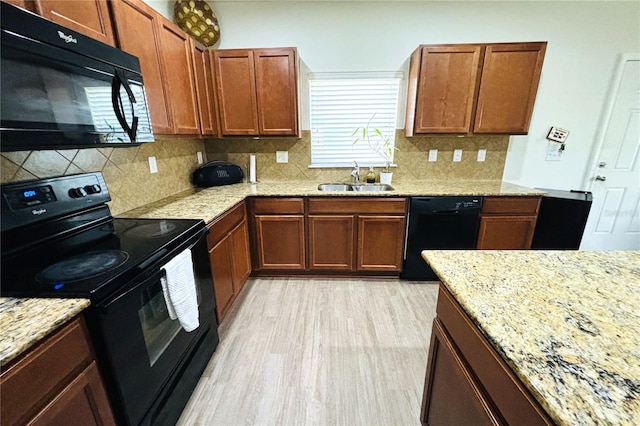 kitchen with light stone counters, sink, tasteful backsplash, black appliances, and light hardwood / wood-style flooring