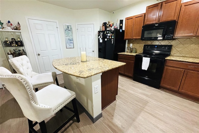 kitchen with backsplash, a center island, light wood-type flooring, and black appliances