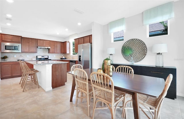 kitchen featuring a kitchen island, backsplash, stainless steel appliances, light tile flooring, and a kitchen breakfast bar