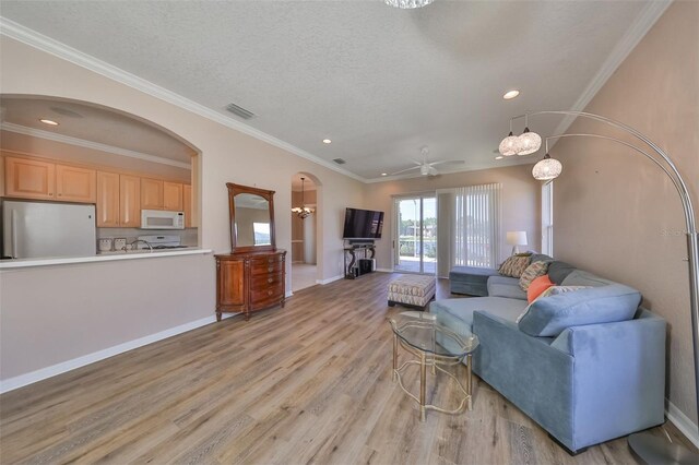 living area with arched walkways, ornamental molding, a textured ceiling, light wood-type flooring, and baseboards