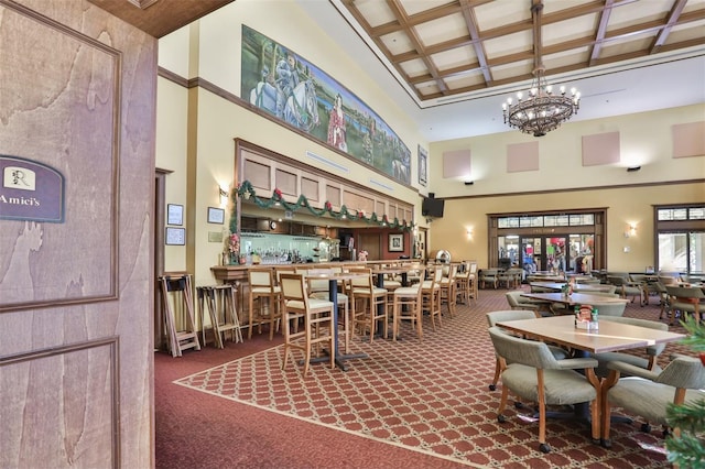 dining space featuring carpet, beam ceiling, a high ceiling, a chandelier, and coffered ceiling