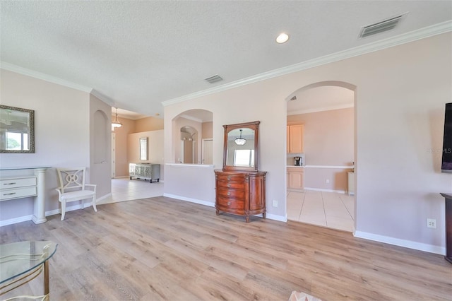 unfurnished living room with arched walkways, ornamental molding, visible vents, and light wood-style floors