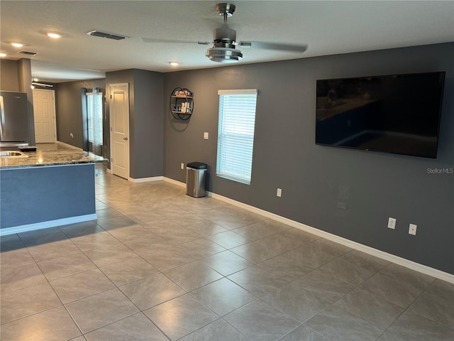 kitchen with tile flooring, light stone counters, stainless steel refrigerator, and ceiling fan