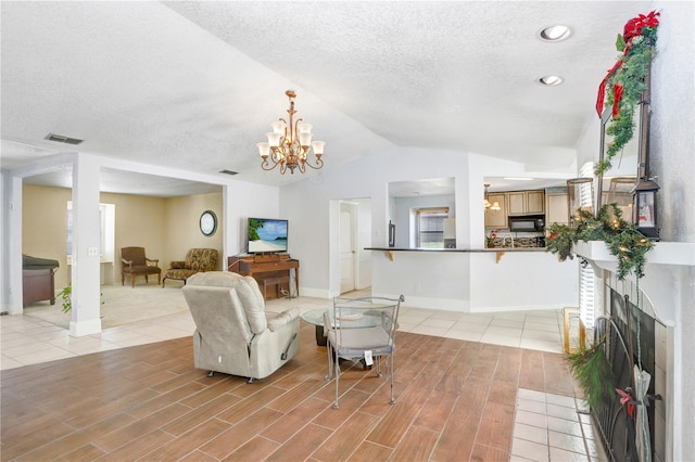 living room featuring a high end fireplace, lofted ceiling, a textured ceiling, a notable chandelier, and light wood-type flooring