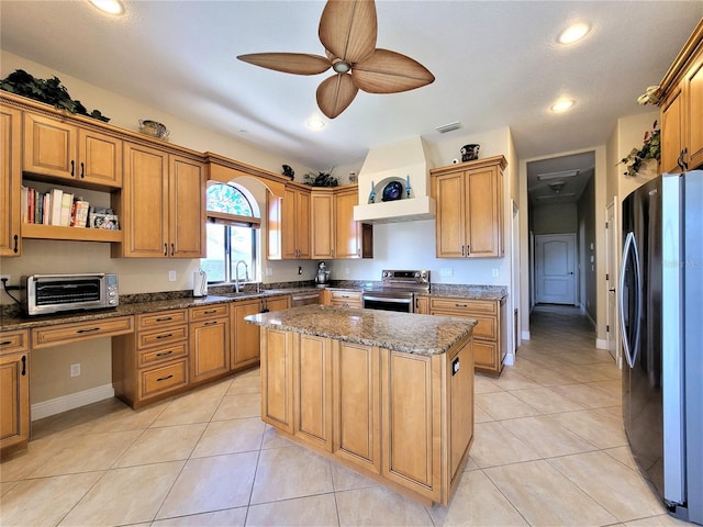 kitchen featuring dark stone counters, a kitchen island, appliances with stainless steel finishes, light tile patterned floors, and ceiling fan