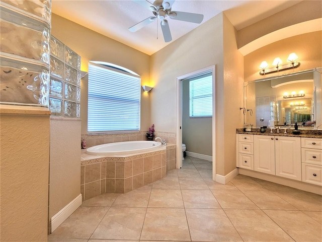 bathroom with ceiling fan, vanity, toilet, a relaxing tiled tub, and tile patterned flooring