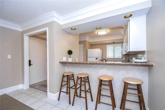 kitchen featuring a kitchen breakfast bar, crown molding, white refrigerator, and kitchen peninsula