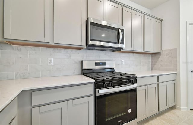 kitchen featuring tasteful backsplash, light stone counters, light tile patterned floors, appliances with stainless steel finishes, and gray cabinets