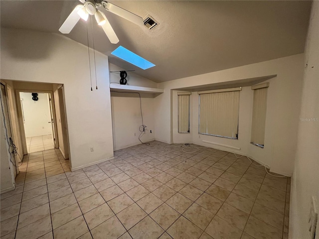 empty room with vaulted ceiling with skylight, light tile flooring, and ceiling fan