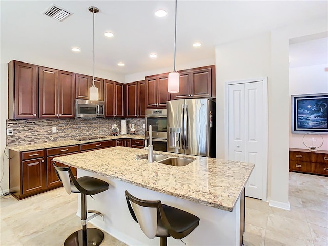 kitchen with decorative light fixtures, sink, appliances with stainless steel finishes, and an island with sink