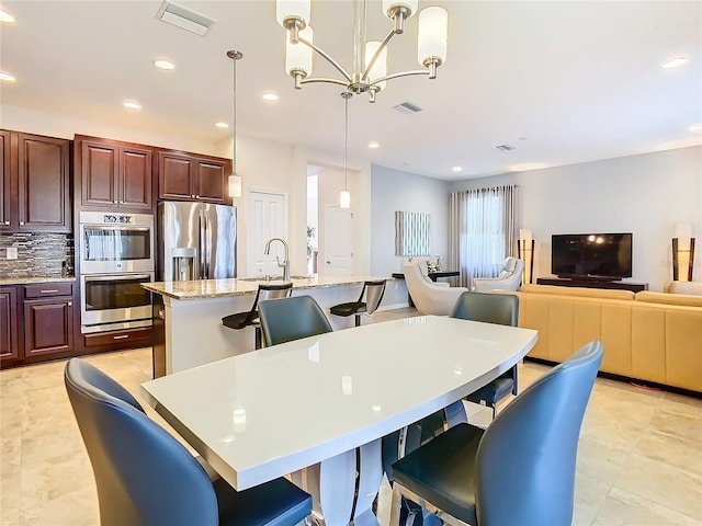 kitchen with a kitchen bar, appliances with stainless steel finishes, backsplash, decorative light fixtures, and light tile flooring