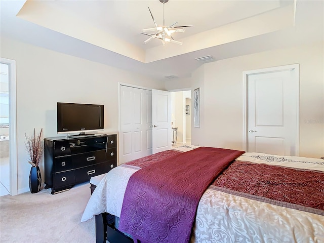 bedroom with connected bathroom, light carpet, ceiling fan, and a tray ceiling