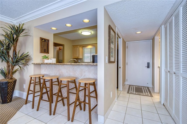 kitchen featuring light brown cabinets, light tile floors, a textured ceiling, kitchen peninsula, and a kitchen breakfast bar