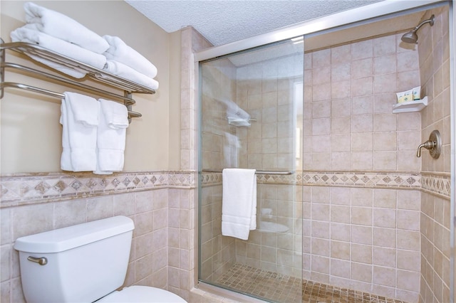 bathroom featuring walk in shower, toilet, tile walls, and a textured ceiling