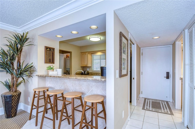 kitchen featuring a kitchen breakfast bar, light brown cabinets, light tile floors, and a textured ceiling