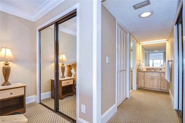 hallway with ornamental molding, sink, light colored carpet, and a textured ceiling