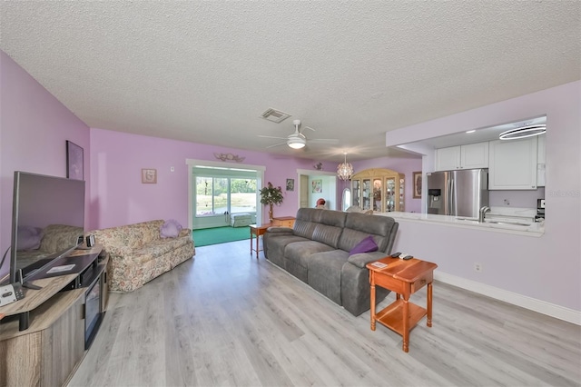 living room with baseboards, light wood-style flooring, visible vents, and a textured ceiling