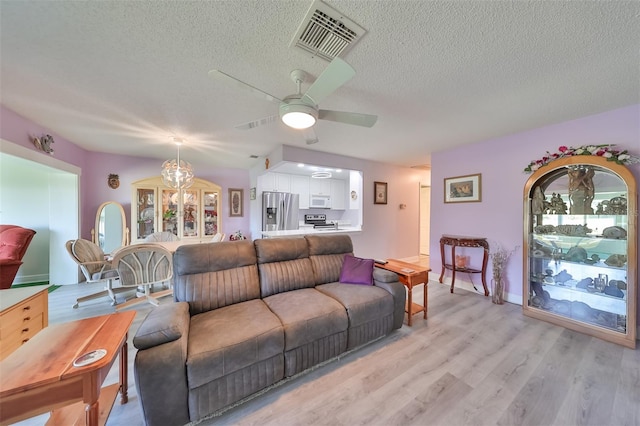 living room with light wood-style flooring, visible vents, ceiling fan, and a textured ceiling