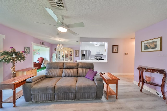 living room with light wood finished floors, a textured ceiling, visible vents, and a ceiling fan