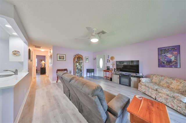 living room featuring a textured ceiling, light wood finished floors, visible vents, and baseboards