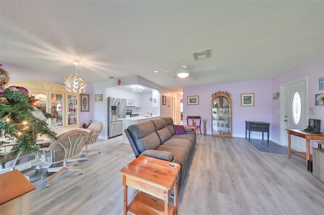 living room featuring a textured ceiling, light wood finished floors, visible vents, and baseboards