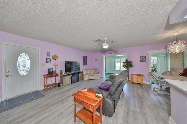 living area featuring light wood-type flooring, visible vents, a textured ceiling, and baseboards