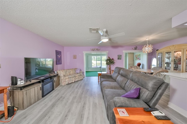 living room featuring light wood-type flooring, visible vents, a textured ceiling, and ceiling fan with notable chandelier