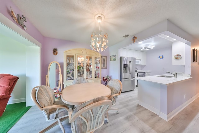 dining area featuring a textured ceiling, light hardwood / wood-style floors, a notable chandelier, and sink