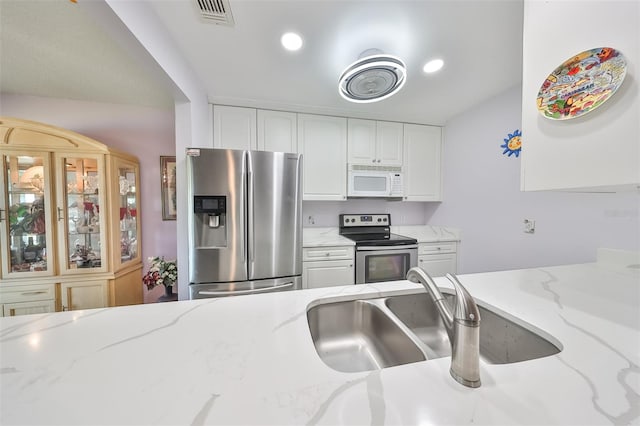 kitchen featuring light stone counters, visible vents, appliances with stainless steel finishes, white cabinetry, and a sink