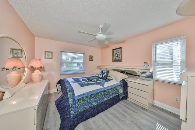 bedroom with light wood finished floors, ceiling fan, baseboards, and a textured ceiling