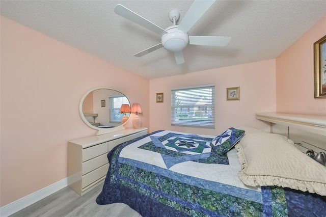 bedroom featuring a textured ceiling, baseboards, a ceiling fan, and light wood-style floors