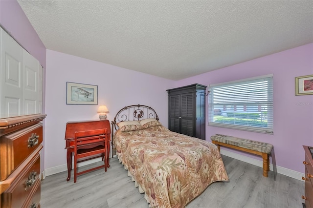 bedroom with light wood-type flooring, a textured ceiling, and baseboards