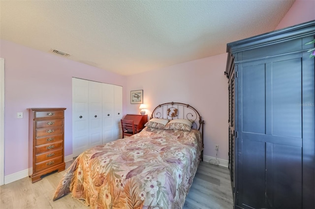 bedroom featuring a textured ceiling, light wood-style flooring, visible vents, baseboards, and a closet