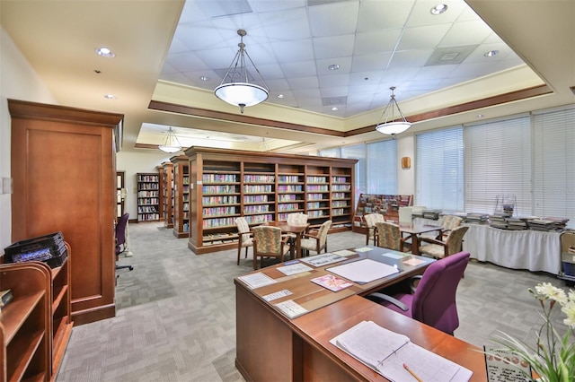 office space featuring a tray ceiling, wall of books, and light colored carpet