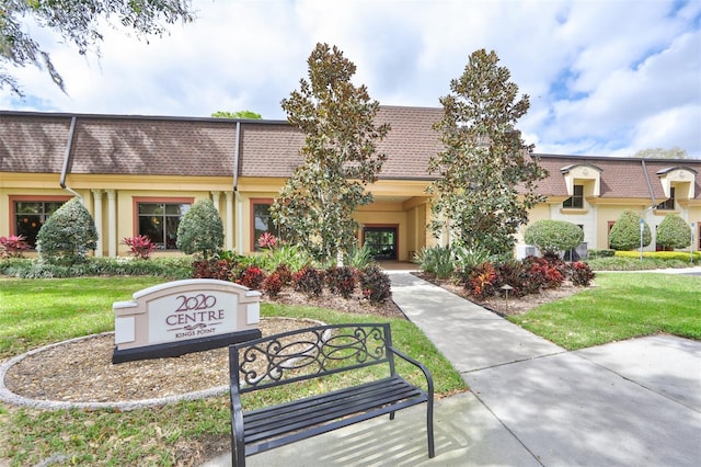 view of property featuring a shingled roof, a front yard, stucco siding, and mansard roof