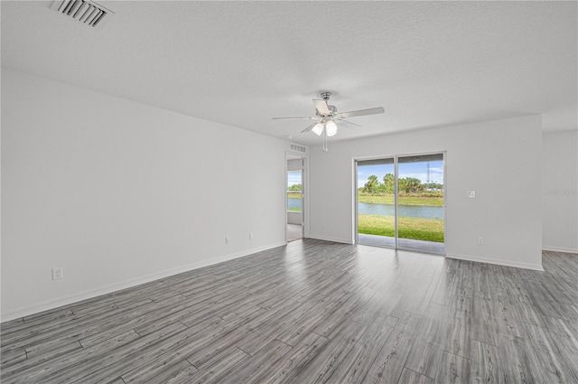 empty room featuring light hardwood / wood-style flooring, a textured ceiling, a water view, and ceiling fan