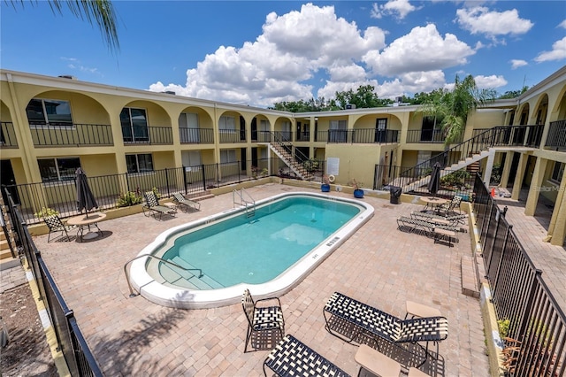 pool with a patio area, stairs, and fence