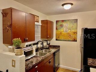 kitchen featuring baseboards, dishwasher, dark countertops, freestanding refrigerator, and a sink