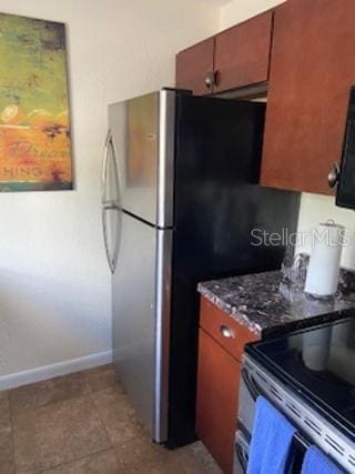 kitchen with light tile patterned floors, baseboards, freestanding refrigerator, brown cabinets, and electric range oven