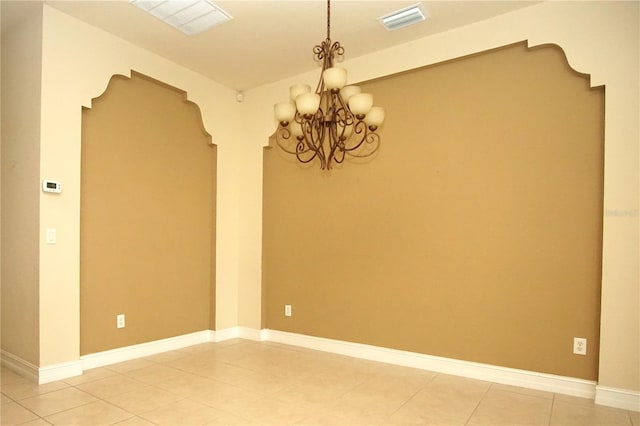 tiled spare room featuring an inviting chandelier