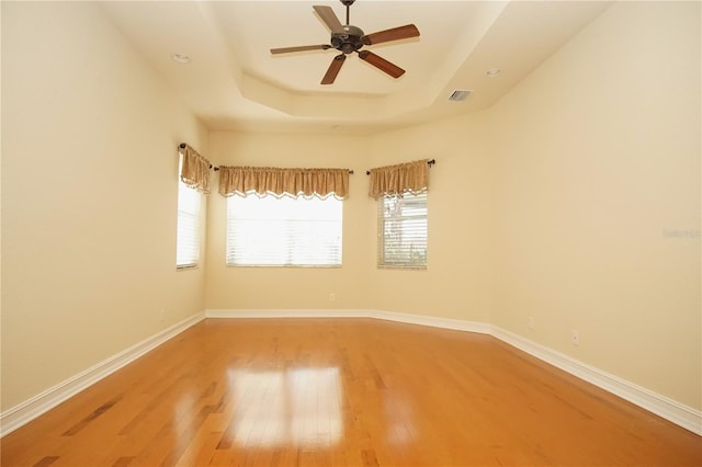 empty room with ceiling fan, a raised ceiling, and wood-type flooring