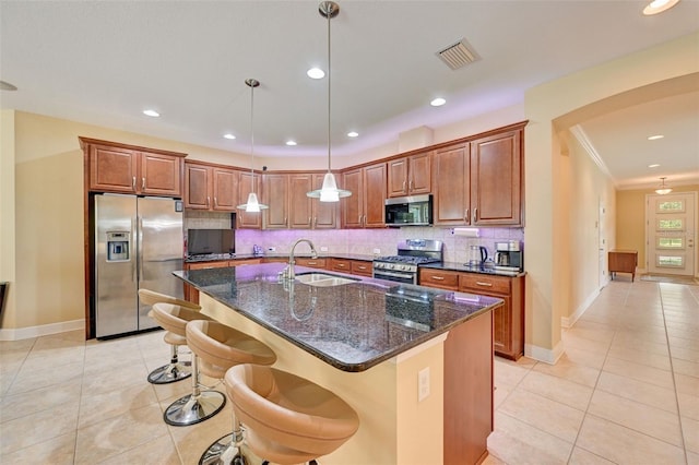 kitchen featuring sink, light tile patterned floors, an island with sink, appliances with stainless steel finishes, and decorative light fixtures