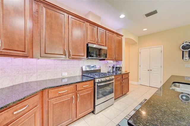 kitchen with backsplash, stainless steel appliances, sink, light tile patterned floors, and dark stone countertops